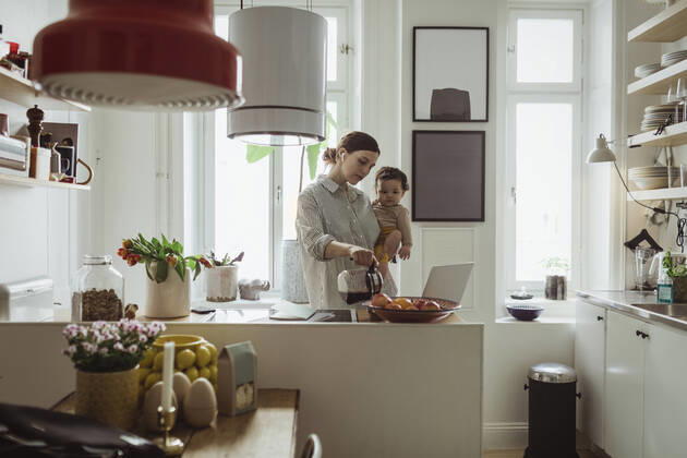 IMAGO Creative, Internationaler Frauenmonat, Entrepreneurinnen Female professional pouring coffee while carrying toddler son in kitchen Sweden, Stockholm, model released, property released Copyright: xMaskotx , MA86822