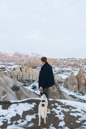 Back view of unrecognizable man in warm clothes with loyal dog in snowy hill against misty mountains in overcast weather in Turkey, Model released Copyright: xCarlosxForteax MR