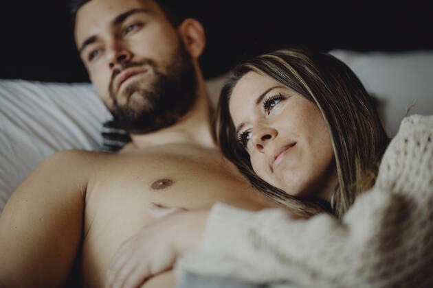 Cheerful young man and woman smiling and cuddling while lying on comfortable bed at home together, Model released Copyright: xMiguelxVallsx MR
