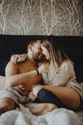 Cheerful young man and woman smiling and cuddling while lying on comfortable bed at home together, Model released Copyright: xMiguelxVallsx MR