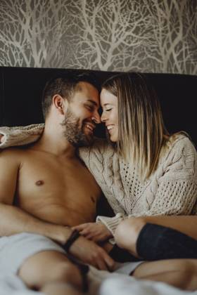 Cheerful young man and woman smiling and cuddling while lying on comfortable bed at home together, Model released Copyright: xMiguelxVallsx MR