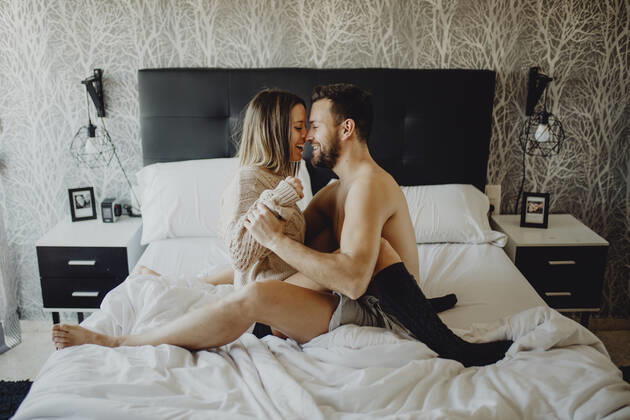 Cheerful young man and woman smiling and cuddling while sitting on comfortable bed at home together, Model released Copyright: xMiguelxVallsx MR