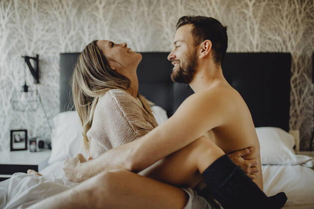 Cheerful young man and woman smiling and cuddling while sitting on comfortable bed at home together, Model released Copyright: xMiguelxVallsx MR