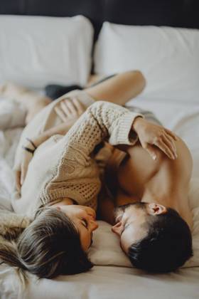 Cheerful young man and woman smiling and cuddling while lying on comfortable bed at home together, Model released Copyright: xMiguelxVallsx MR