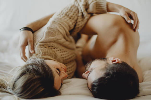Cheerful young man and woman smiling and cuddling while lying on comfortable bed at home together, Model released Copyright: xMiguelxVallsx MR