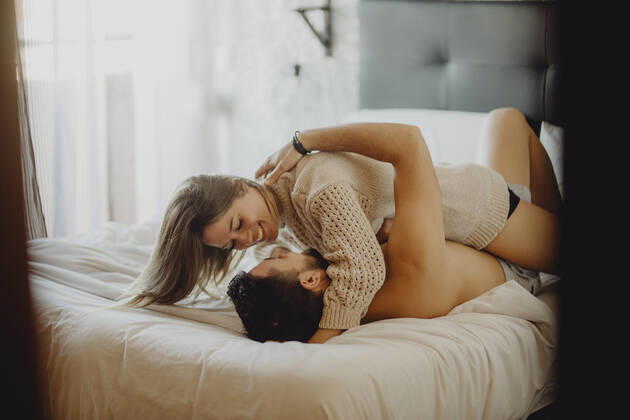 Cheerful young man and woman smiling and cuddling while lying on comfortable bed at home together, Model released Copyright: xMiguelxVallsx MR