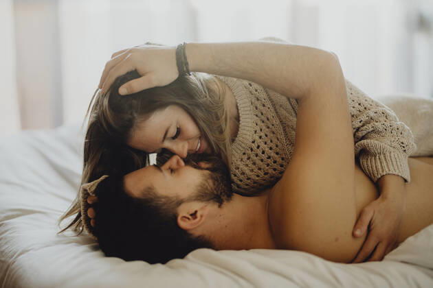 Cheerful young man and woman smiling and cuddling while lying on comfortable bed at home together, Model released Copyright: xMiguelxVallsx MR