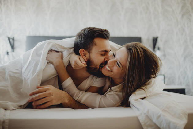 Cheerful young man and woman smiling and cuddling while lying on comfortable bed at home together, Model released Copyright: xMiguelxVallsx MR