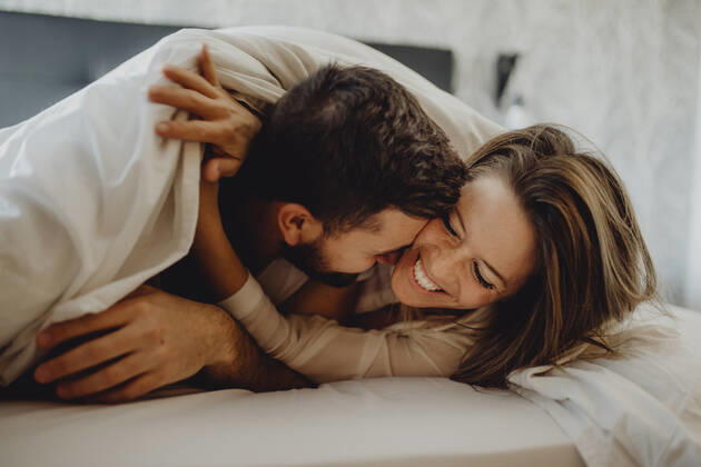 Cheerful young man and woman smiling and cuddling while lying on comfortable bed at home together, Model released Copyright: xMiguelxVallsx MR
