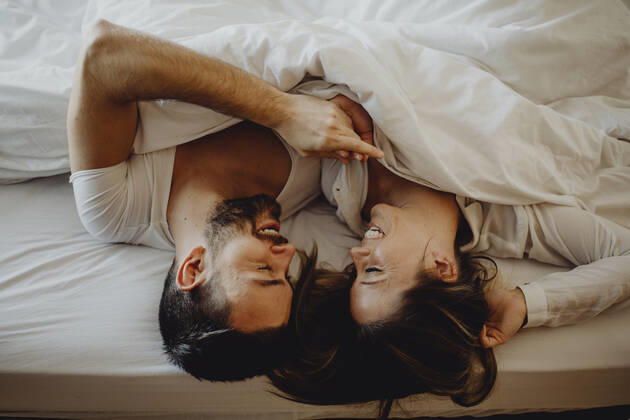 Cheerful young man and woman smiling and cuddling while lying on comfortable bed at home together, Model released Copyright: xMiguelxVallsx MR