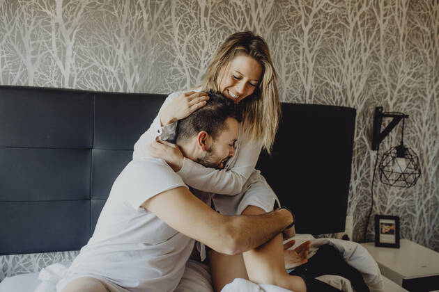 Cheerful young man and woman smiling and cuddling while sitting on comfortable bed at home together, Model released Copyright: xMiguelxVallsx MR