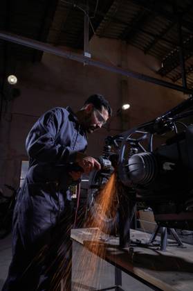 Bearded worker in overall using angle grinder while polishing metal details of custom motorcycle in workshop Copyright: xPhilippexDegrootex Model Released