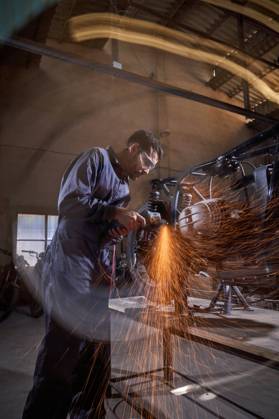 Bearded worker in overall using angle grinder while polishing metal details of custom motorcycle in workshop Copyright: xPhilippexDegrootex Model Released