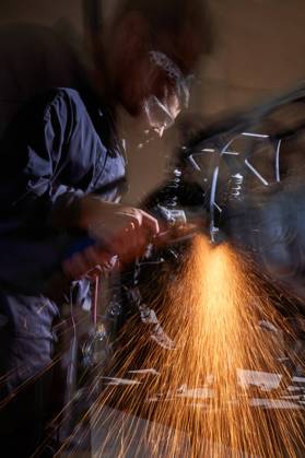 Bearded worker in overall using angle grinder while polishing metal details of custom motorcycle in workshop Copyright: xPhilippexDegrootex Model Released