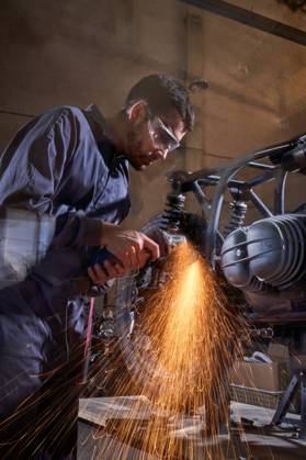 Bearded worker in overall using angle grinder while polishing metal details of custom motorcycle in workshop Copyright: xPhilippexDegrootex Model Released