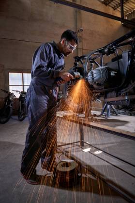 Bearded worker in overall using angle grinder while polishing metal details of custom motorcycle in workshop Copyright: xPhilippexDegrootex Model Released