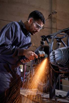 Bearded worker in overall using angle grinder while polishing metal details of custom motorcycle in workshop Copyright: xPhilippexDegrootex Model Released