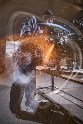 Bearded worker in overall using angle grinder while polishing metal details of custom motorcycle in workshop Copyright: xPhilippexDegrootex Model Released