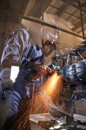 Bearded worker in overall using angle grinder while polishing metal details of custom motorcycle in workshop Copyright: xPhilippexDegrootex Model Released