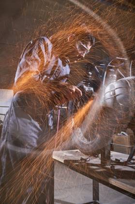 Bearded worker in overall using angle grinder while polishing metal details of custom motorcycle in workshop Copyright: xPhilippexDegrootex Model Released