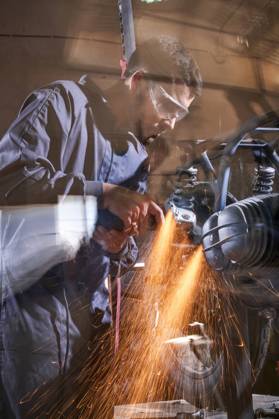 Bearded worker in overall using angle grinder while polishing metal details of custom motorcycle in workshop Copyright: xPhilippexDegrootex Model Released