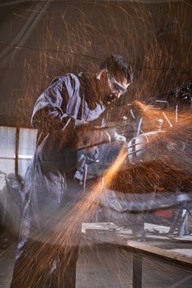 Bearded worker in overall using angle grinder while polishing metal details of custom motorcycle in workshop Copyright: xPhilippexDegrootex Model Released