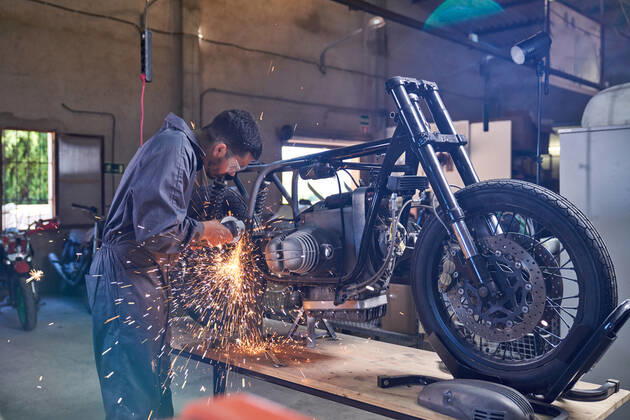 Bearded worker in overall using angle grinder while polishing metal details of custom motorcycle in workshop Copyright: xPhilippexDegrootex Model Released