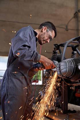 Bearded worker in overall using angle grinder while polishing metal details of custom motorcycle in workshop Copyright: xPhilippexDegrootex Model Released