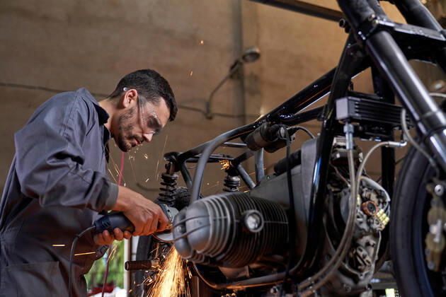 Bearded worker in overall using angle grinder while polishing metal details of custom motorcycle in workshop Copyright: xPhilippexDegrootex Model Released
