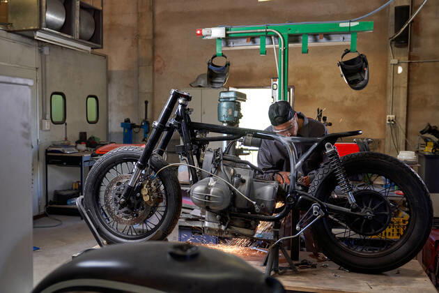 Bearded worker in overall using angle grinder while polishing metal details of custom motorcycle in workshop Copyright: xPhilippexDegrootex Model Released