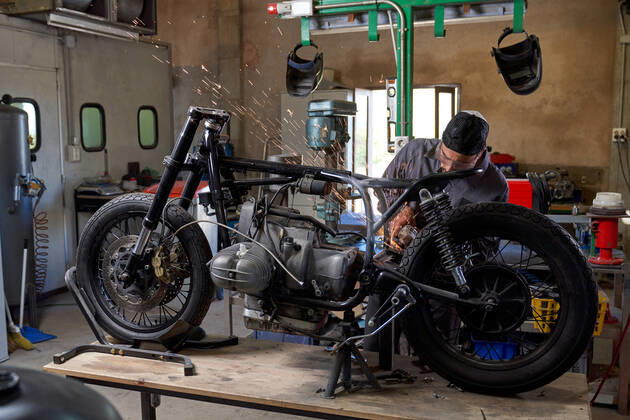 Bearded worker in overall using angle grinder while polishing metal details of custom motorcycle in workshop Copyright: xPhilippexDegrootex Model Released