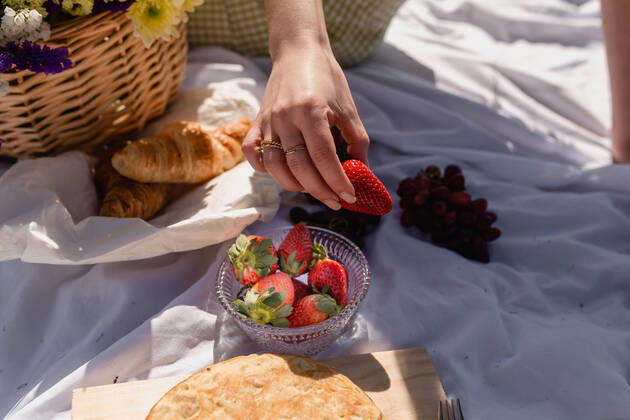 IMAGO Creative: Jahreszeit Fr?hling, Picknick High angle of crop female with ripe strawberry having picnic with croissant and grapes with focaccia, Model released Copyright: xAnaxCarpiox MR