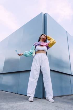 Confident female wearing jeans with top and colorful shirt with stylish sunglasses standing near wall, Model released Copyright: xJosexDexJesusxSaldanax MR