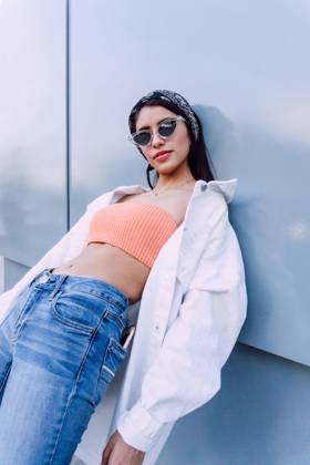 Confident female wearing jeans with top and white shirt with stylish sunglasses standing near wall, Model released Copyright: xJosexDexJesusxSaldanax MR