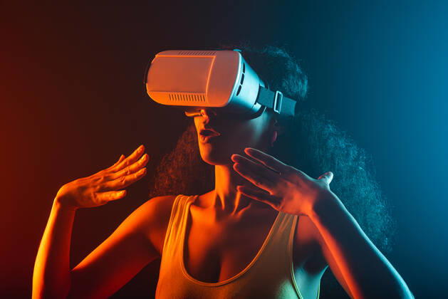 Anonymous astonished ethnic female with open mouth exploring virtual reality in headset on black background, Model released Copyright: xLeonardoxBorgesx MR