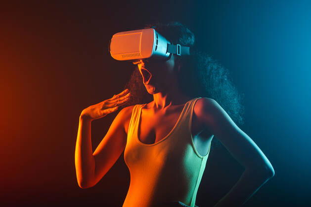 Anonymous astonished ethnic female with open mouth exploring virtual reality in headset on black background, Model released Copyright: xLeonardoxBorgesx MR
