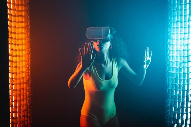 Anonymous astonished ethnic female with open mouth exploring virtual reality in headset on black background, Model released Copyright: xLeonardoxBorgesx MR