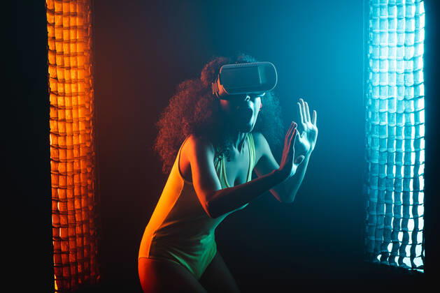 Anonymous astonished ethnic female with open mouth exploring virtual reality in headset on black background, Model released Copyright: xLeonardoxBorgesx MR