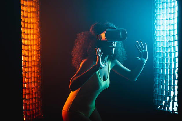 Anonymous astonished ethnic female with open mouth exploring virtual reality in headset on black background, Model released Copyright: xLeonardoxBorgesx MR