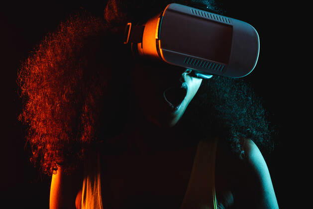 Anonymous astonished ethnic female with open mouth exploring virtual reality in headset on black background, Model released Copyright: xLeonardoxBorgesx MR