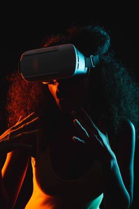 Anonymous astonished ethnic female with open mouth exploring virtual reality in headset on black background, Model released Copyright: xLeonardoxBorgesx MR