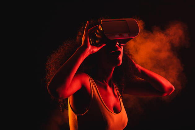 Anonymous astonished ethnic female with open mouth exploring virtual reality in headset on black background, Model released Copyright: xLeonardoxBorgesx MR