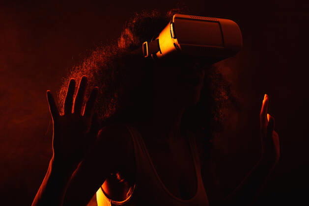 Anonymous astonished ethnic female with open mouth exploring virtual reality in headset on black background, Model released Copyright: xLeonardoxBorgesx MR