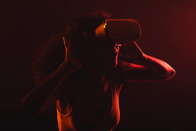 Anonymous astonished ethnic female with open mouth exploring virtual reality in headset on black background, Model released Copyright: xLeonardoxBorgesx MR