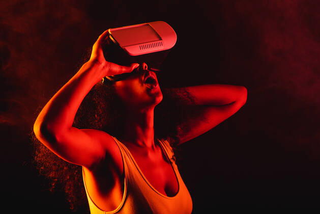 Anonymous astonished ethnic female with open mouth exploring virtual reality in headset on black background, Model released Copyright: xLeonardoxBorgesx MR