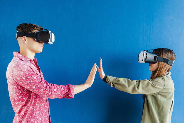 Friends with virtual reality headset stretching hands towards each other by blue wall model released Symbolfoto DLTSF01842