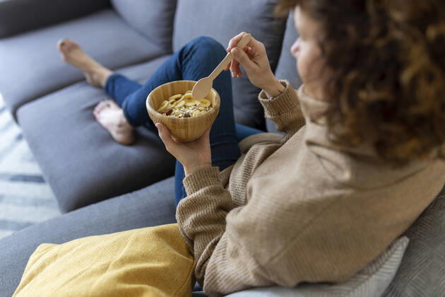 IMAGO Creative: Jahreszeit Winter, Couching Woman with food bowl in living room at home model released Symbolfoto property released JPTF00770
