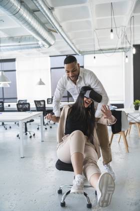 Businessman pushing cheerful female colleague using wearable computer sitting on chair in office model released Symbolfoto property released SNF01243