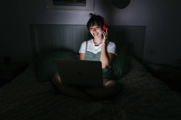 Smiling woman wearing headphones using laptop at home model released Symbolfoto property released TCEF01773