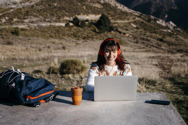 Smiling woman wearing headphones using laptop at mountain model released Symbolfoto TCEF01774